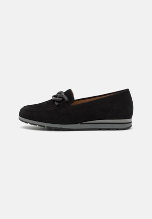 Sorte suede loafers med grå gummisål og stor sort kædedetalje på forsiden, vist i profil på en hvid baggrund.