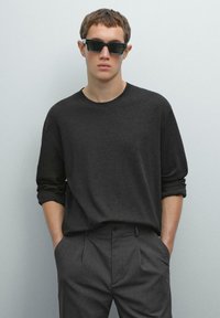 Donkergrijze lange mouwen t-shirt gecombineerd met gestreepte broek. Het shirt heeft een ronde hals en een ontspannen pasvorm. Vierkante zwarte zonnebril gedragen.