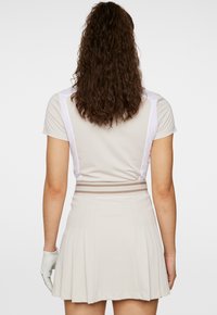 Beige idrottstopp med vita accenter och plisserad beige kjol. Har en strukturerad midjeband med två horisontella ränder. Handske på vänster hand.