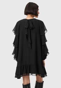 Abito nero con maniche a volant fluide e dettaglio di legatura sul retro. Il tessuto sembra leggero e con una finitura texture. L'orlo è a strati e svasato.