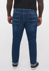 Jeans din denim albastru, cu croială dreaptă, având două buzunare pe spate cu cusături contrastante. Margini cu manșetă și purtați cu adidași negri.