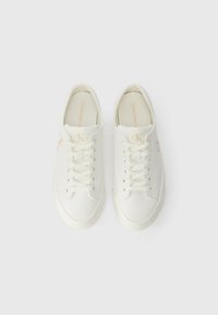 White canvas sneakers with tonal laces, rounded toe, Calvin Klein logo in light beige on side, cushioned insole, rubber sole.