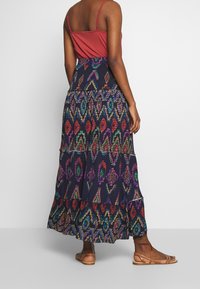 Maxikjol med ett flerfärgat geometriskt mönster på en marinblå botten, med tierade lager och midjeresår. Tillsammans med en röd linne och sandaler.