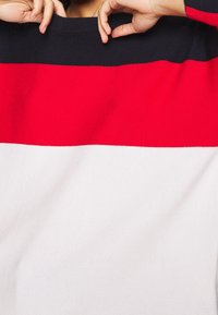 Stickad tröja med horisontella ränder i marinblått, rött och vitt. Ribbad textur med rundad hals och lös passform.