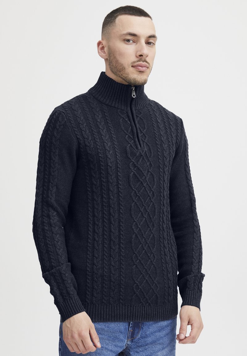 Maglione nero a coste con collo alto e mezzo zip, caratterizzato da motivi testurizzati e polsini e orlo a coste. I jeans in denim completano il look.