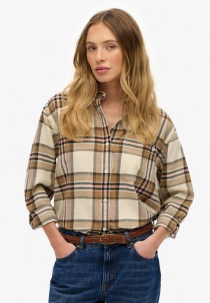 Beige and brown plaid shirt with button-up front, long sleeves, and a relaxed fit, paired with a woven brown belt and blue jeans.