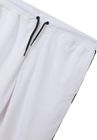 Pantaloni jogger bianchi con coulisse nera e strisce laterali nere a contrasto. Realizzati in tessuto leggero, con tasche laterali e vita elastica.