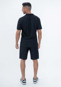 Chemise polo noire et short assorti en tissu léger. L'ensemble se compose de manches courtes, d'une coupe droite, et de chaussures de tennis avec des accents blancs.