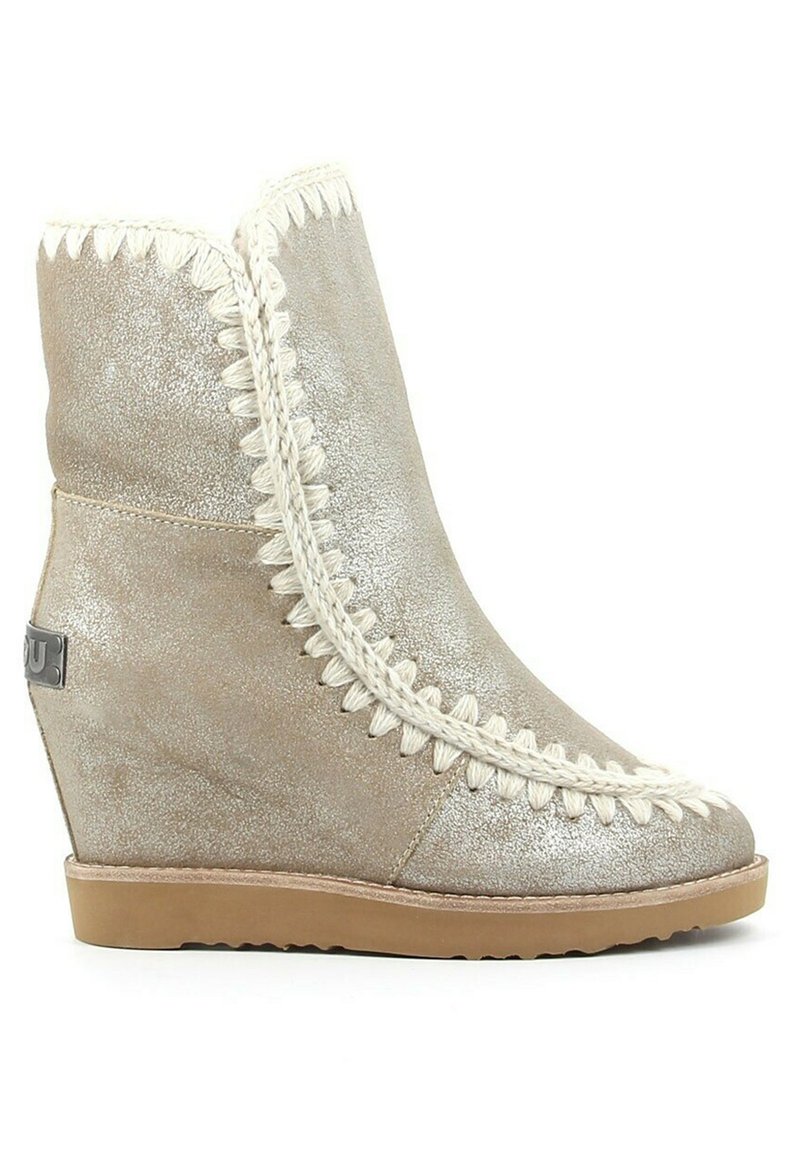 Wedge enkellaarsjes in metallic goudleer met decoratieve witte stitching langs de rand, een gestructureerde bovenkant en een bruine rubberen zool.