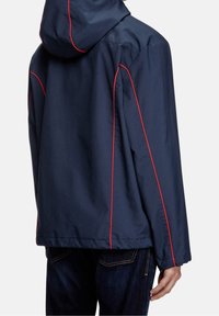 Granatowa kurtka z kapturem, z czerwoną lamówką wzdłuż szwów. Gładka tekstura, lekki materiał i luźny krój.