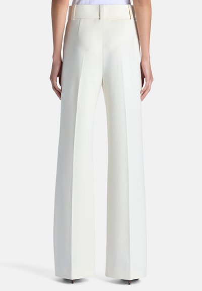 Femme portant un pantalon blanc taille haute à jambes larges vue de dos, avec passants de ceinture et plis marqués sur chaque jambe.