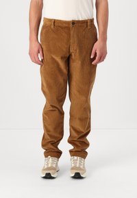 Brune kordfløjlsbukser med lige pasform, der har en knappelukning foran og sidelommer, parret med lyse sneakers.