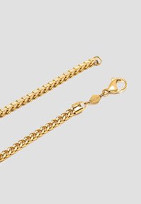 Guldkæde med sammenkoblede led, en struktureret overflade og en hulklap-lås med et sekskantet mærke.