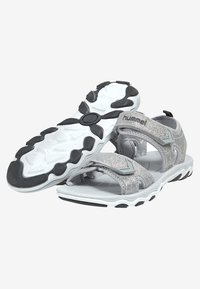Grå atletiska sandaler med en texturerad ovandel, justerbara Velcro-remmar och en vit, flexibel gummisula med svarta accenter.