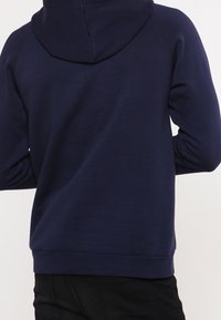 Tmavě modrá mikina s klokaní kapsou, žebrovaným lemem a manžetami a kapucí. Vyrobena z měkké, texturované látky s pohodlným střihem.