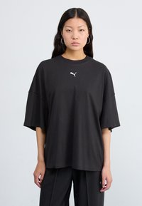 Svart oversized t-skjorte laget av bomull, med korte ermer og rund hals. Lite hvitt logo på brystet. Glatt tekstur, uformell design.