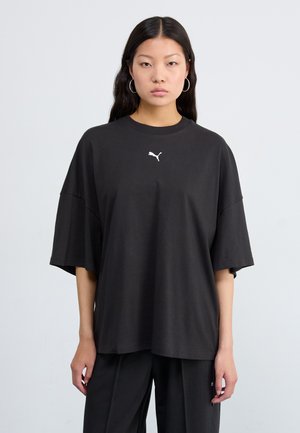 Black oversized t-shirt made of cotton, featuring short sleeves and a round neck. Small white logo on the chest. Smooth texture, casual design.