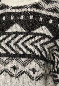 Stickad tröja med ett svart och vitt geometriskt mönster, med en mjuk textur och rund halsringning. Framträdande zigzag- och diamantmotiv.