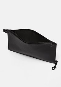 Pochette rectangulaire en cuir noir avec une fermeture éclair sur le dessus et un petit fermoir en métal sur le côté, présentée ouverte sur un fond blanc.