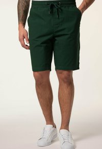 Shorts en coton verts avec une taille à cordon de serrage, des poches latérales et une coupe droite. Associés à des baskets blanches.