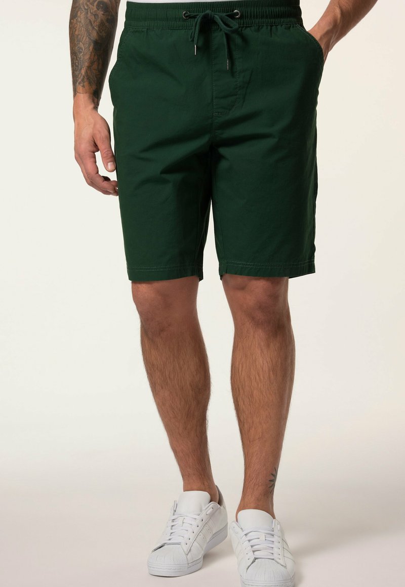 Shorts en coton verts avec une taille à cordon de serrage, des poches latérales et une coupe droite. Associés à des baskets blanches.