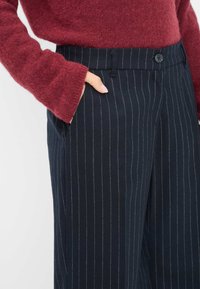 Marineblauwe gestreepte broek met een getailleerde pasvorm, gemaakt van een gladde stof. Voorzien van een knoopsluiting en zakken, gecombineerd met een bordeauxkleurige wollen trui.