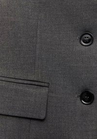 Szary materiał garniturowy o gładkiej fakturze, z dwoma czarnymi guzikami i pojedynczą klapkową kieszenią z precyzyjnym przeszyciem.