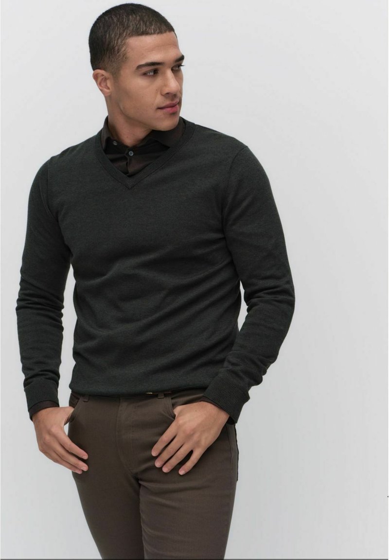 Mörkgrå v-halsad tröja i mjukt tyg, med långa ärmar och ribbade muddarna, kombinerad med bruna skräddarsydda byxor.