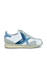 Zapatilla blanca con acentos de ante gris claro y detalles de cuero azul. Cuenta con un diseño de cordones y una suela curvada. Logo "Munich" presente.