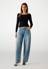 Maglietta nera a maniche lunghe abbinata a jeans a gamba larga di colore blu chiaro. Il tessuto della maglietta è liscio; i jeans presentano una finitura sfumata con una vestibilità comoda.