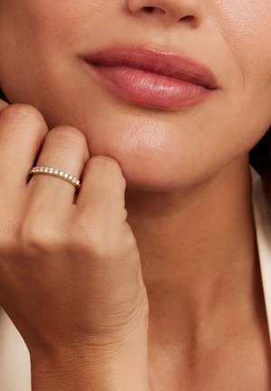 Gros plan sur les lèvres et le bas du visage avec une main près du menton portant une bague en or sertie de petits diamants à l'annulaire.