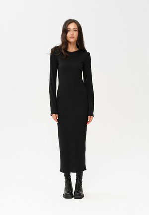 Černé žebrované šaty s dlouhým rukávem, kulatým výstřihem, přiléhavým střihem a délkou po kotníky, doplněné černými kozačkami po kolena.