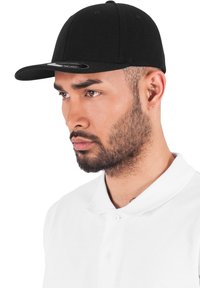 Fekete baseball sapka, ívelt karimával, szövetből készült, sima tapintású és minimális varrással rendelkezik, fehér galléros inggel viselve.
