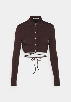Braun geschnittenes Langarmshirt mit Kragen, ausgestattet mit silbernen Knöpfen und einem Bindeband in der Taille. Glatter Stoff mit taillierter Passform.