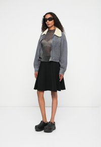 Halli hallide gamasärk shearling kaelusega, läbipaistev metallist top, must flared seelik ja mustad ventilatsiooniaukudega klotsid.