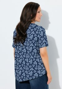 Granatowa bluzka z krótkim rękawem z białym wzorem liści, z zaokrąglonym dołem, wykonana z miękkiej tkaniny, pokazana od tyłu.