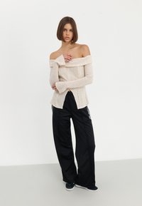 Beige strikket topp med avskåret skuldre og lange ermer, satt sammen med svarte, vide joggebukser med hvite side-striper og avslappet passform.