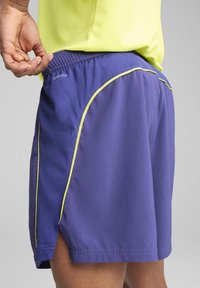 Lila Sportshorts mit einer leichten Textur, versehen mit einer gelben Akzentnaht und einem elastischen Bund. Das „DRYCELL“-Logo ist sichtbar.
