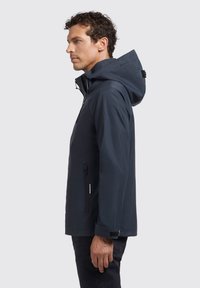 La chaqueta impermeable azul marino cuenta con una capucha resistente, un bolsillo con cremallera y puños ajustables. Está fabricada con un material suave y resistente a las inclemencias del tiempo.