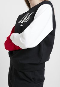 Black, white, and red sweatshirt with long sleeves. Features bold lettering on the front. Material appears soft and textured.