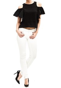 Top negro de hombros descubiertos con mangas con volantes, combinado con jeans skinny blancos. La modelo lleva zapatos de tacón negros. Diseño y ajuste simples.