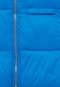 Chaqueta de plumas azul con cierre de cremallera y un pequeño bolsillo en el pecho. Presenta una textura suave y brillante, así como secciones acolchadas para aislamiento.