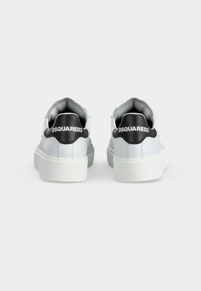Paire de baskets blanches avec des semelles épaisses, des languettes de talon noires et le logo "DSQUARED2" imprimé en blanc à l’arrière de chaque chaussure.
