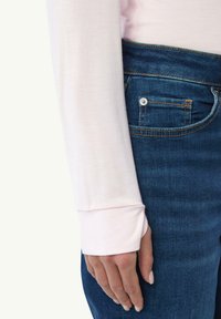 Hellrosa Langarmshirt mit einer weichen Textur und eng anliegenden Manschetten. Kombiniert mit dunkelblauen Jeans aus Denim mit sichtbaren Nähten und Taschendetails.