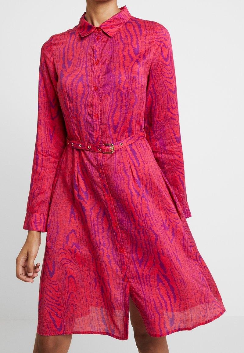 Abito camicia rosa a maniche lunghe con colletto, caratterizzato da un motivo ondulato testurizzato, chiusura con bottoni frontale e cintura abbinata con fibbia dorata.