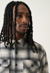 Camicia di flanella a quadri in tonalità di grigio, con colletto abbottonato, due tasche sul petto e tessuto texturizzato con motivi a quadri distinti.