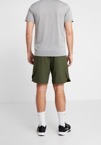 Camiseta deportiva gris, de manga corta, combinada con pantalones cortos de carga verde olivo con bolsillos laterales. Zapatillas deportivas negras y calcetas blancas.