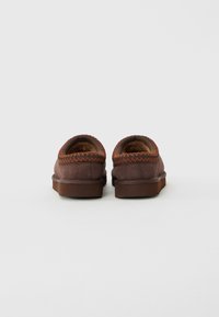 Pair of brown suede slip-on shoes with orange zigzag stitching and thick rubber soles, viewed from the back on a plain background.