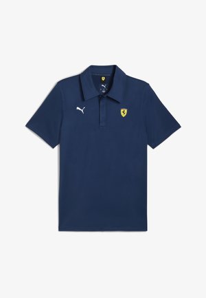 Temno modra polo majica iz mehkega blaga z ovratnikom, kratkimi rokavi, belim logotipom Puma in rumenim grbom Ferrari na prsih.