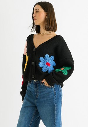 Black knitted cardigan with large embroidered flowers in blue, pink, red, and green. Features a V-neck and buttons down the front.